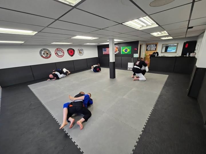 Barrick BJJ students paired up grappling on mats wearing gi uniforms during class.